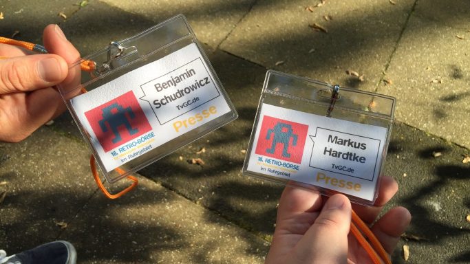 Zwei Namensschilder mit orangem Band, jeweils mit Namen und Logo.